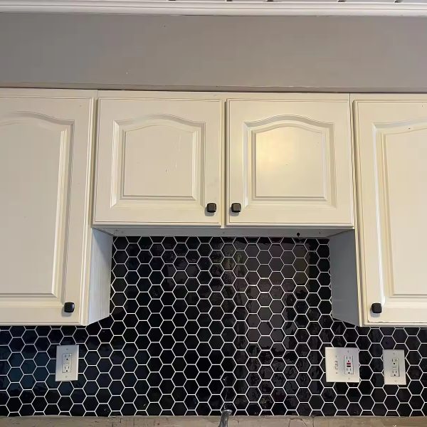 Black Hexagon tile backsplash installed on the wall of a kitchen with off-white wooden cabinets.