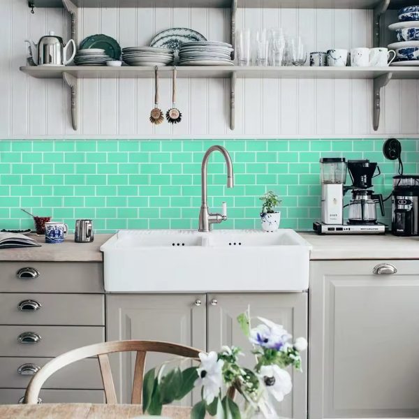 Green Subway tile backsplash installed on the wall of a kitchen with grey wooden cabinets and white wash basin.