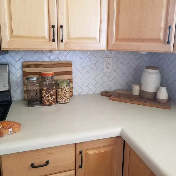 White Argyle Subway tile backsplash installed on the wall of a kitchen with wooden cabinets and white stone countertop.